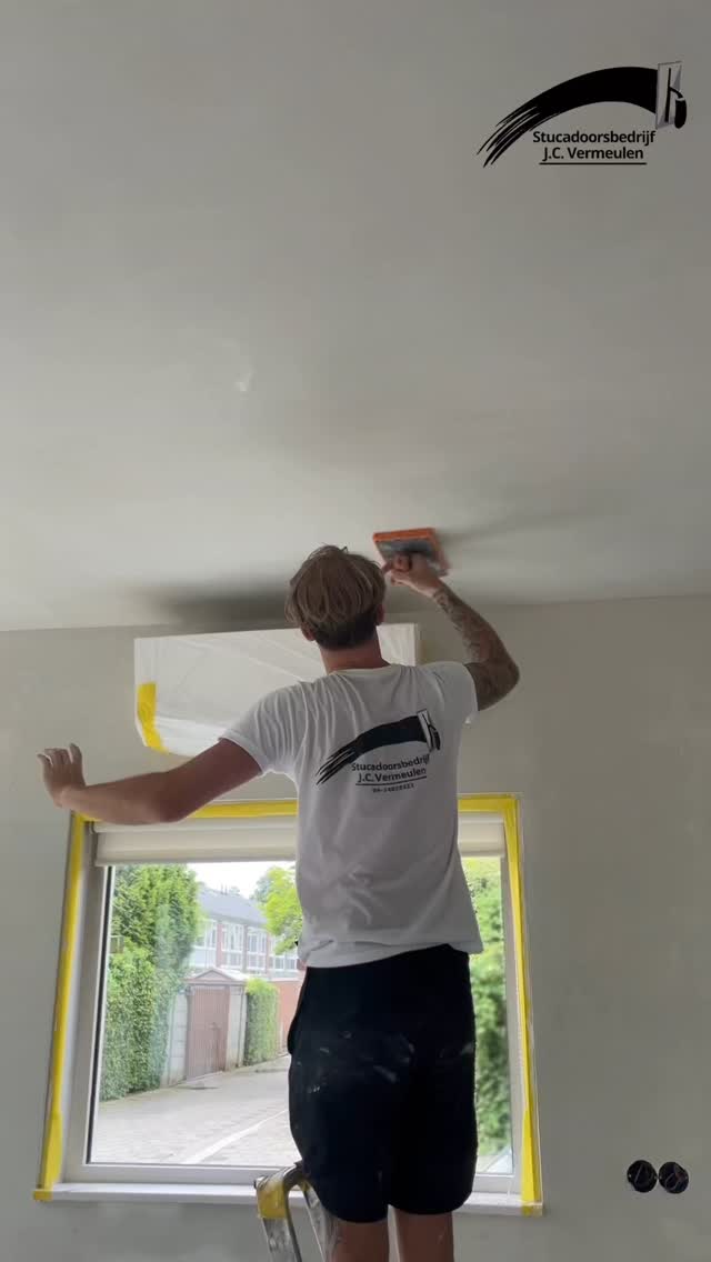JC Vermeulen stuct een plafond langs een afgeplakt kozijn, met de spaan in de hand