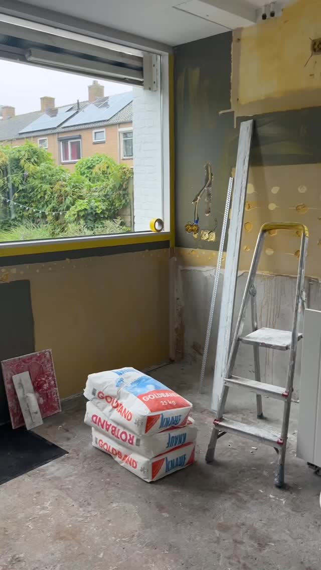 Keuken tijdens de renovatie, met een trapje, zakken stucmateriaal en een groot raam