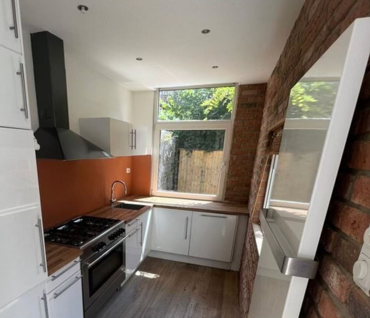 Keuken voor de renovatie, met een oranje muur, een bakstenen hoek en oude kastjes
