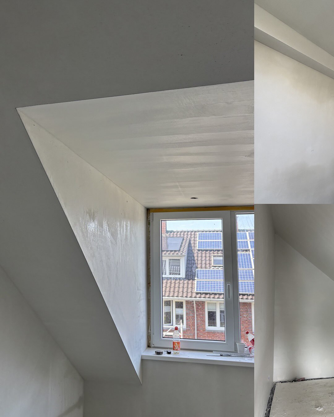 Gestucte zolder met wit plafond en een dakraam met uitzicht op daken met zonnepanelen